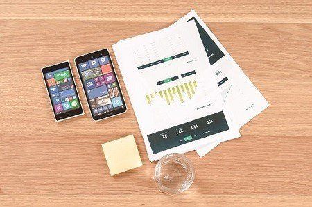 Two phones , sticky notes , and a glass of water are on a wooden table.